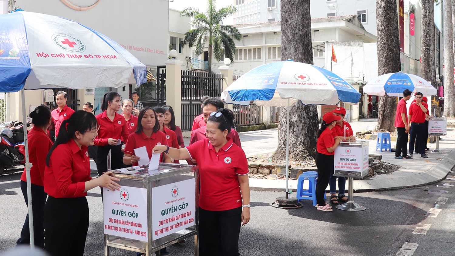 Cán bộ Hội Chữ thập đỏ áo đỏ bỏ tiền ủng hộ vào thùng quyên góp đặt trước trụ sở Hội Chữ thập đỏ Thành phố Hồ Chí Minh
