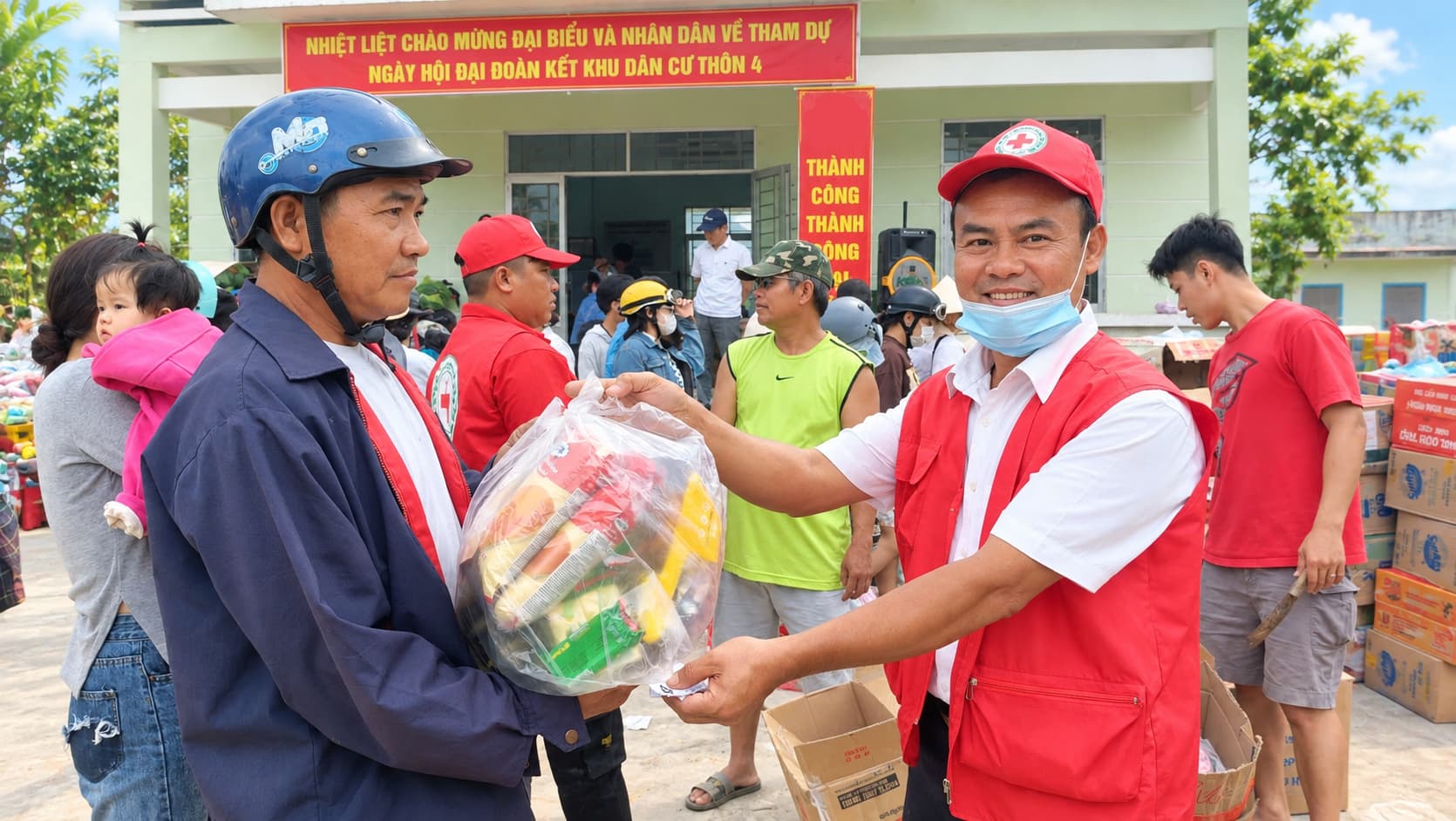 Cán bộ Hội Chữ thập đỏ mặc áo gi-lê đỏ trao túi quà cứu trợ cho người dân tại ngày hội đại đoàn kết khu dân cư